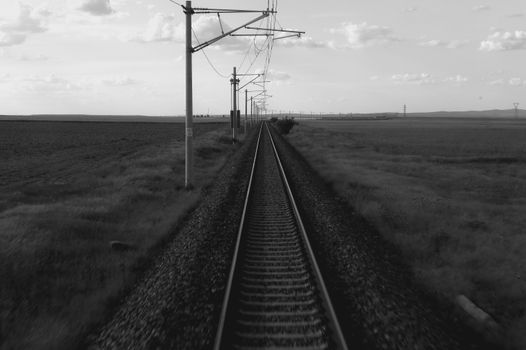A serene black and white view of railway tracks stretching through rural countryside.