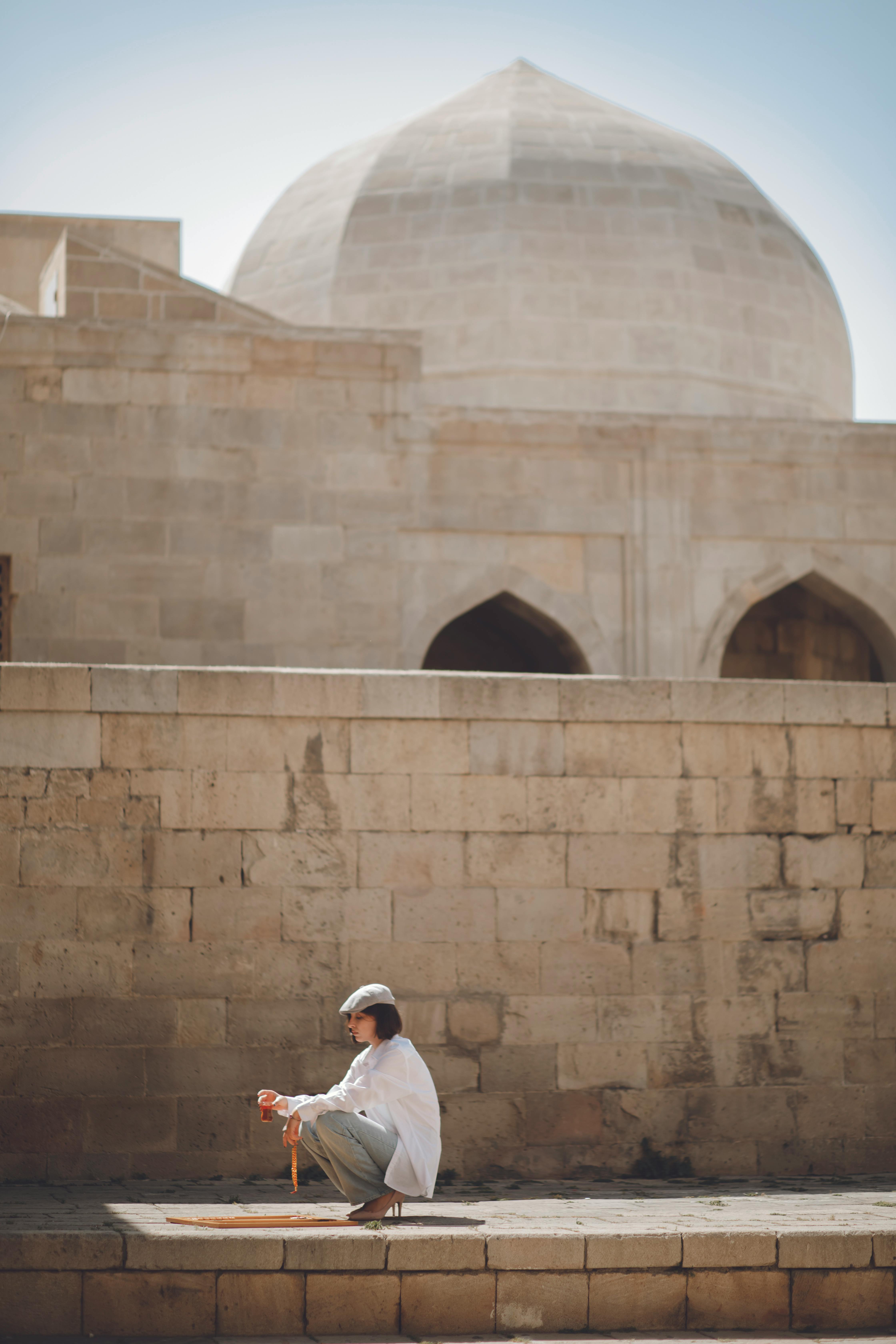 A man sits in contemplation near ancient architecture in Baku, Azerbaijan on a sunny day.