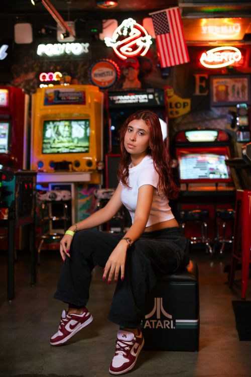 Free Trendy young woman posing amidst vibrant vintage arcade machines, exuding retro vibes. Stock Photo