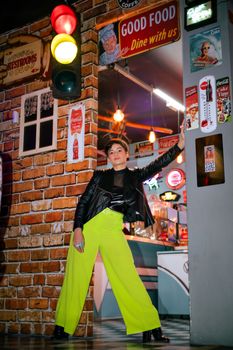 Fashionable woman in bright outfit poses outside a retro diner at night.