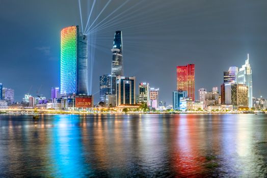 Colorful night view of Ho Chi Minh City skyline with illuminated skyscrapers reflecting on the Saigon River.