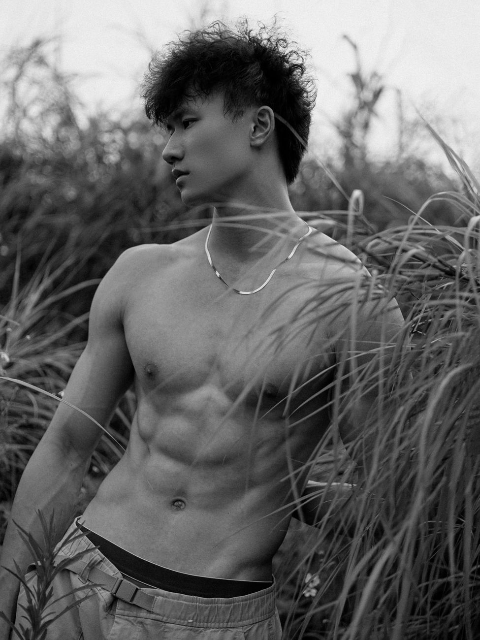 Artistic black and white photo of a shirtless man posing confidently in a grassy field.