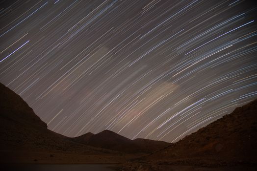 Long exposure photo capturing star trails over mountain silhouette on a clear night.