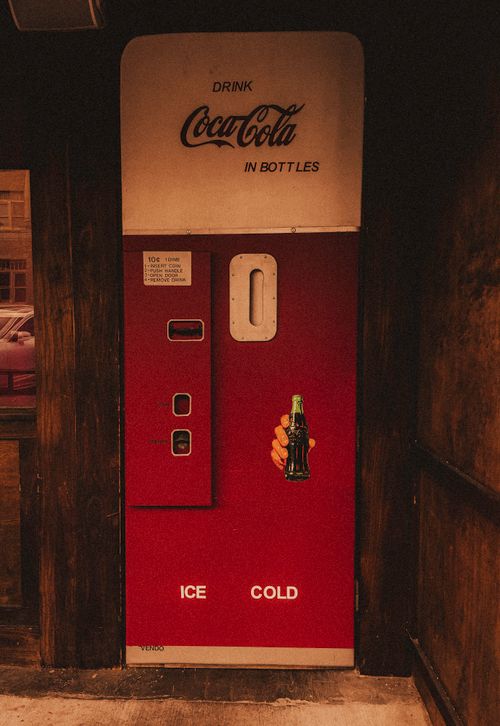 Free Retro Coca-Cola vending machine in a rustic indoor setting, evoking nostalgia. Stock Photo