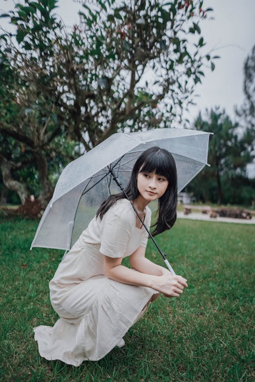Woman Crouching under Transparent Umbrella