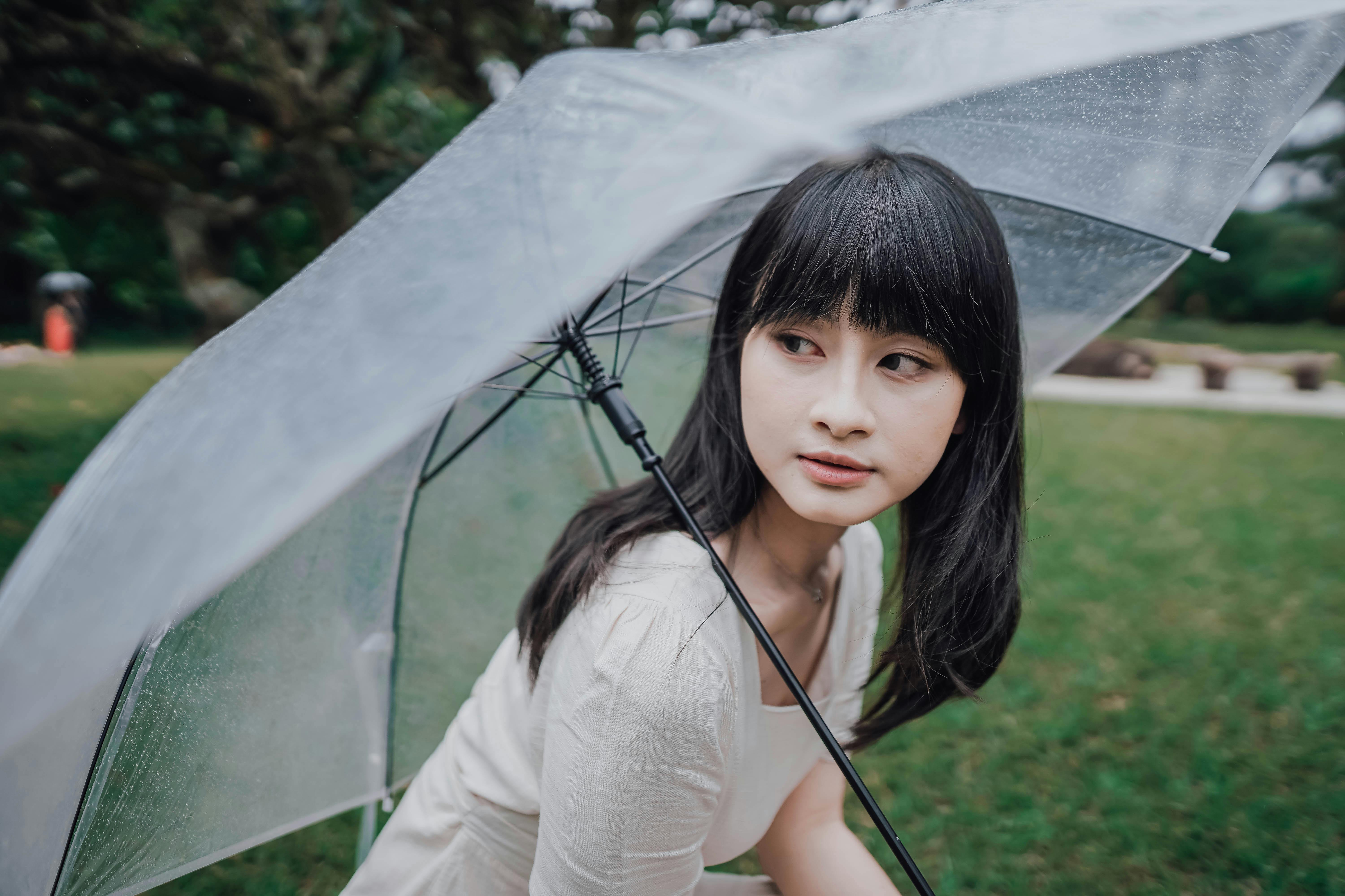 Woman with a transparent umbrella looking to the side in a park setting.