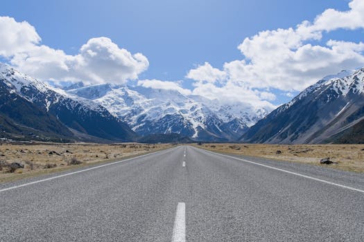 An empty road leading to the snow-capped Aoraki Mount Cook under a clear blue sky in New Zealand.