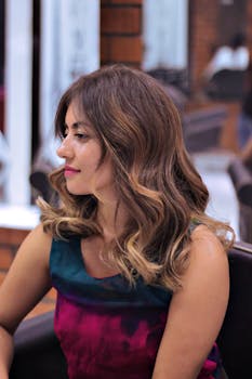 Young woman with elegantly styled brown hair sitting in a salon chair, looking serene.