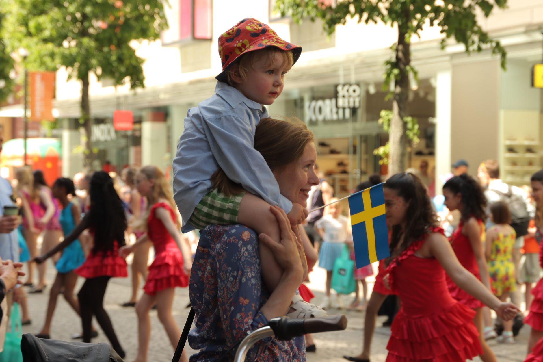 A vibrant street parade in Jönköping, Sweden, with people celebrating and waving the Swedish flag.