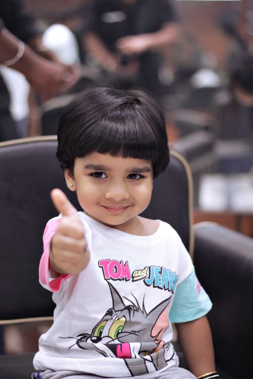 Free Cute child with a Tom and Jerry shirt giving a thumbs up while sitting indoors. Stock Photo