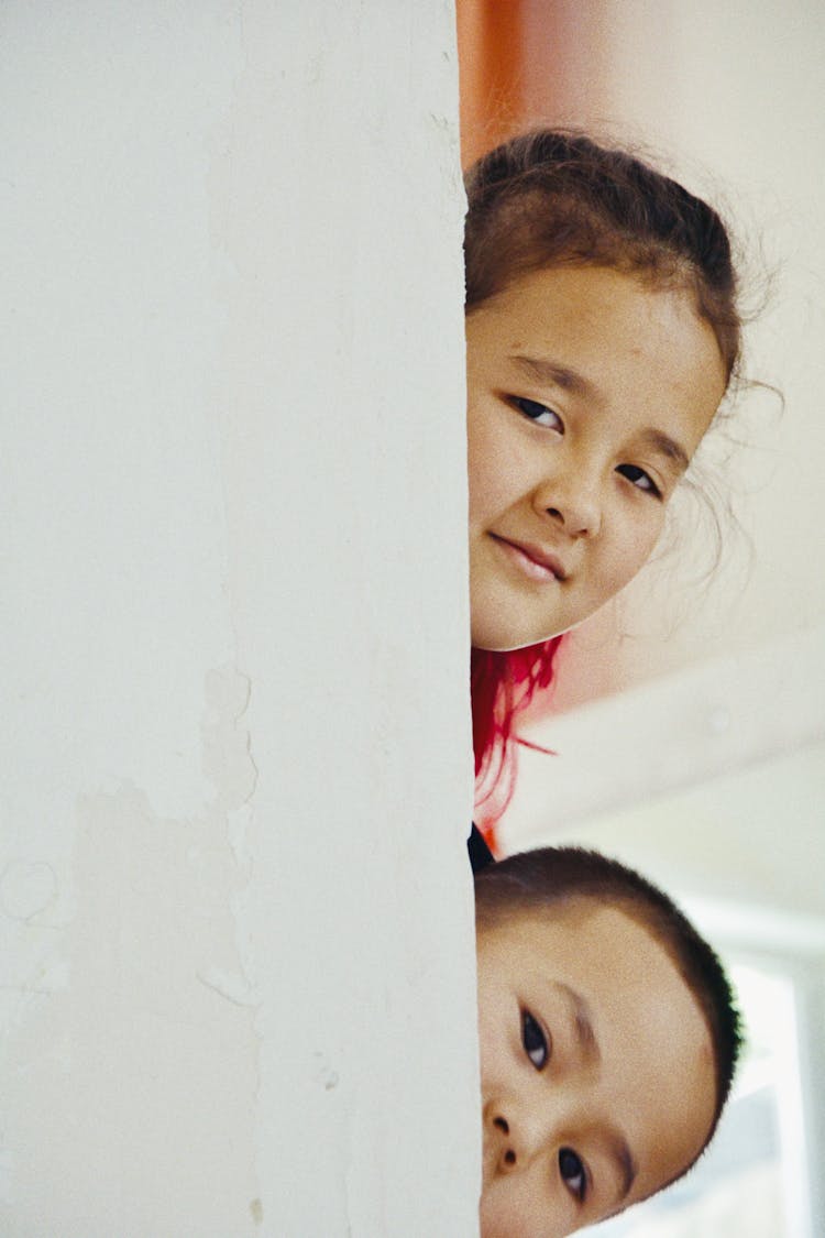 A Little Boy And Girl Peeking From Behind The Wall 