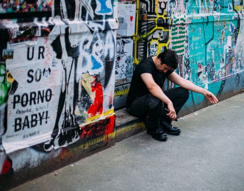 Free Man sitting by colorful graffiti wall, capturing urban street art vibe in a city alleyway. Stock Photo
