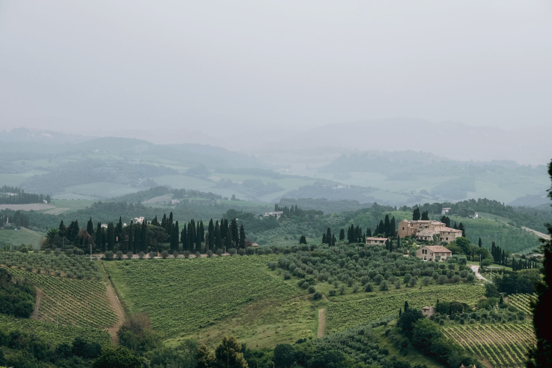 A serene aerial view of a misty Tuscan countryside with verdant hills and a quaint village.