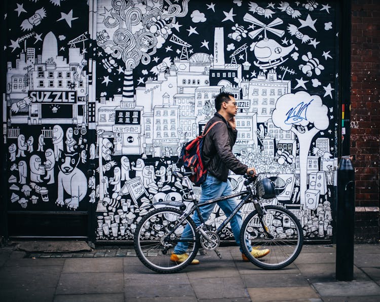 Man In Black Jacket Holding A Black Hardtail Bike Near Black And White Art Wall