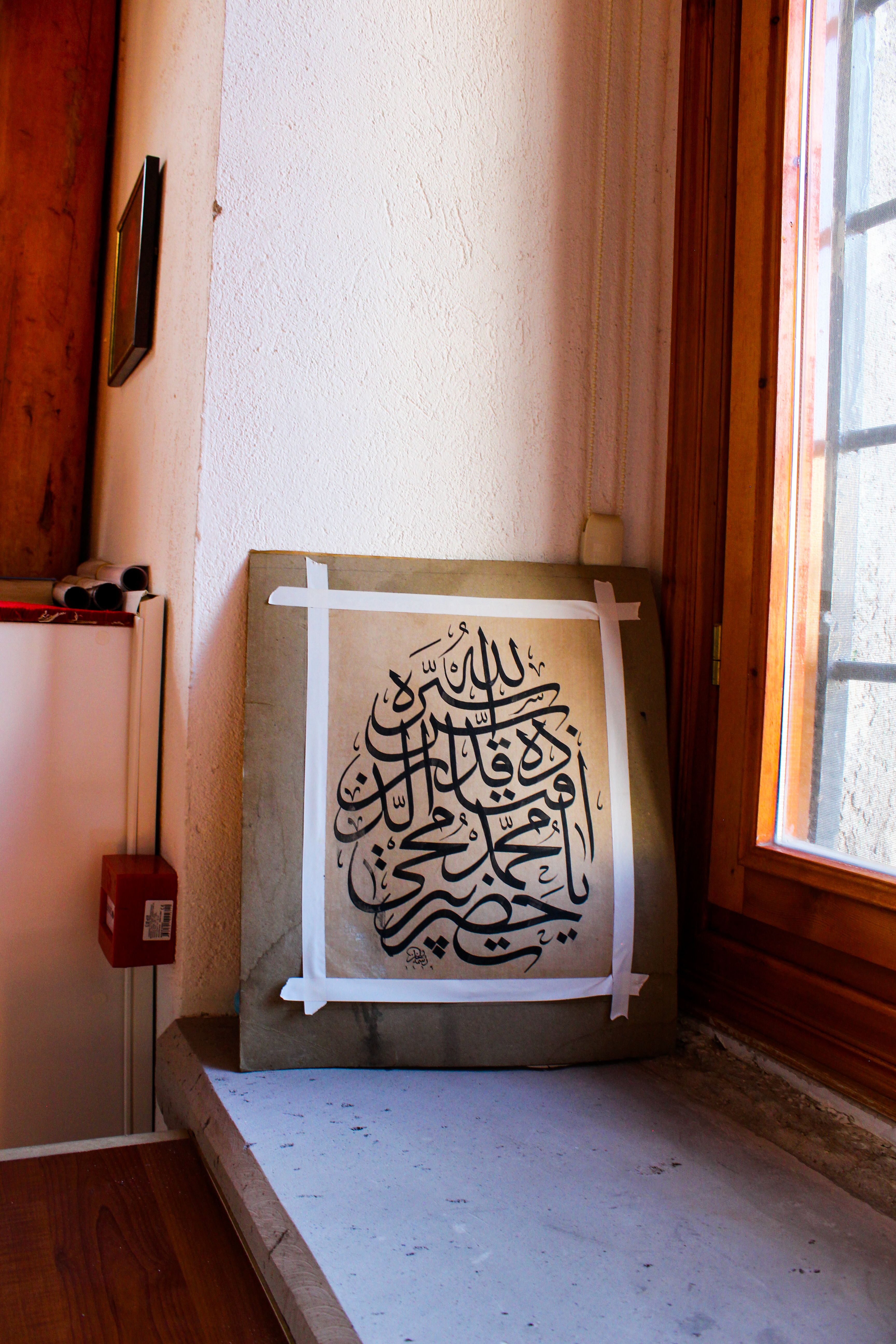 Arabic calligraphy art piece in a sunlit indoor setting, showcasing traditional design.