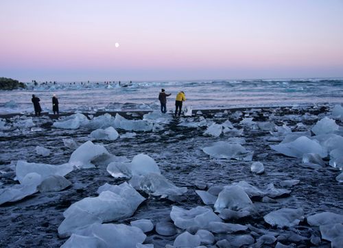 Free Tourists admire ice formations on Jökulsárlón beach in Iceland under a twilight sky. Stock Photo