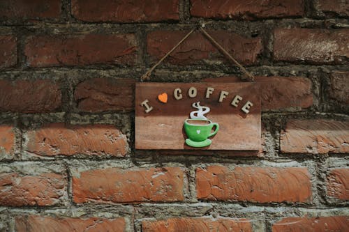 A Wooden Decoration with a Coffee Illustration Hanging on a Red Brick Wall 