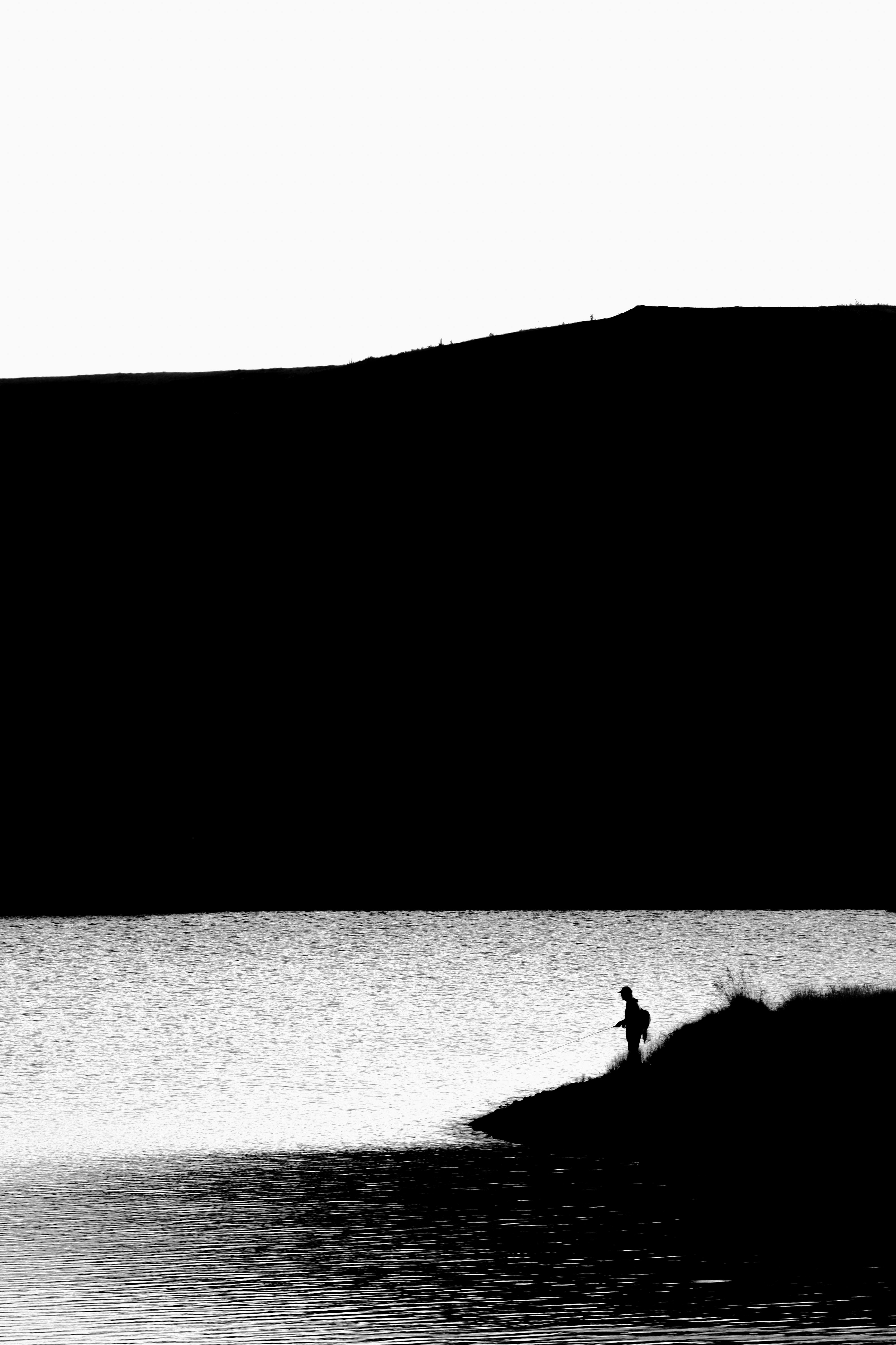 A striking black and white silhouette of a lone fisherman by a tranquil lake.