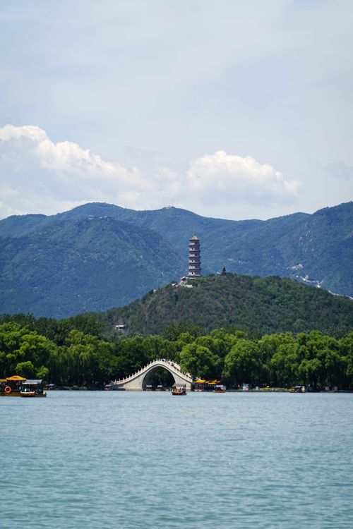 Free Beautiful view of a tower and arched bridge over water in Beijing, surrounded by lush hills and mountains. Stock Photo