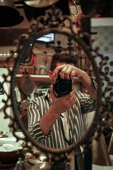 A young man captures a selfie using a digital camera in an ornate antique mirror reflection.