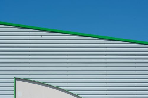 Free Minimalist industrial building facade against a clear blue sky, featuring green accents for striking contrast. Stock Photo