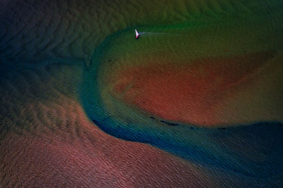 A colorful aerial view of a sailboat navigating the vibrant waters near Exmouth, UK.