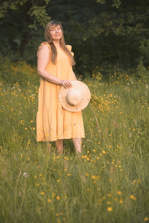 Free A woman in a yellow dress holding a hat stands in a wildflower meadow during summer. Stock Photo