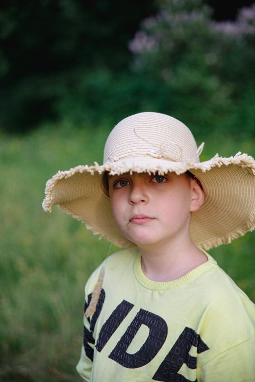Free Portrait of a young boy wearing a straw hat, standing outdoors in a summer meadow. Stock Photo