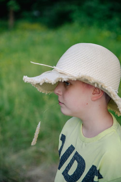 A Boy in a Hat Holding a Straw in His Mouth 