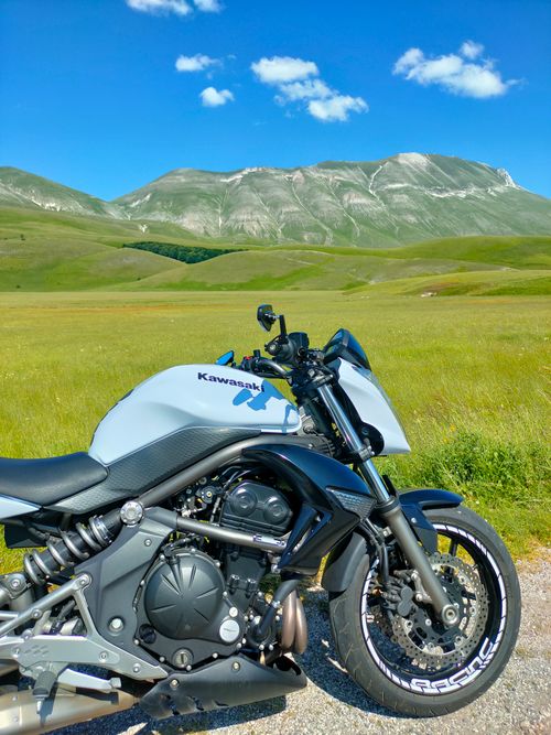 Free A sleek motorcycle parked in a vast field with majestic mountains in the background under a clear blue sky. Stock Photo