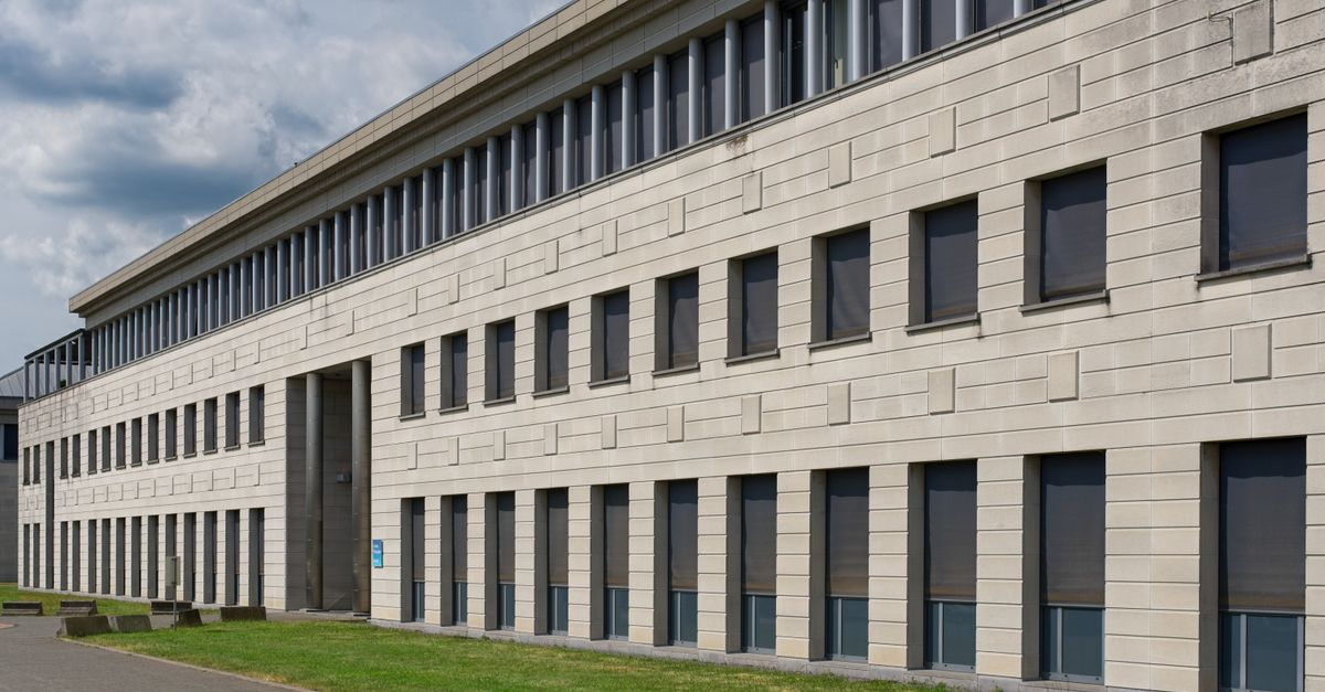 Contemporary building exterior featuring windows, blinds, and grass area in an urban setting.