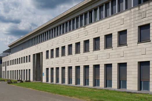 Contemporary building exterior featuring windows, blinds, and grass area in an urban setting.