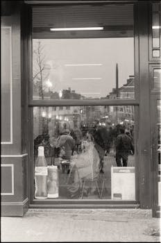 Black and white photo capturing city street reflections in a cafe window.