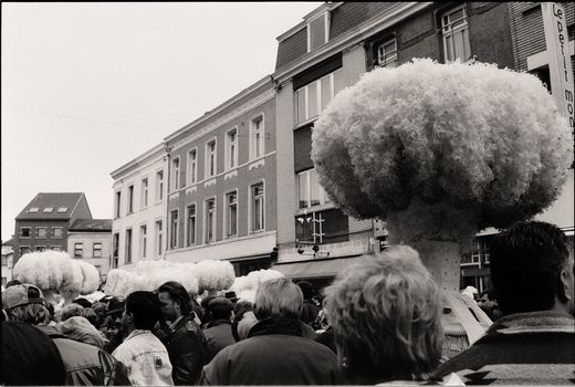 Black and white photo of a festive parade with people wearing large fluffy hats.