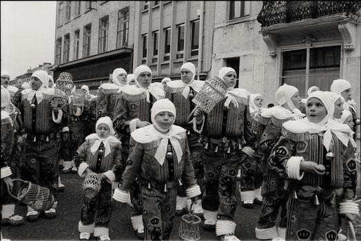 Black and white photo of a traditional city parade with people in costumes.