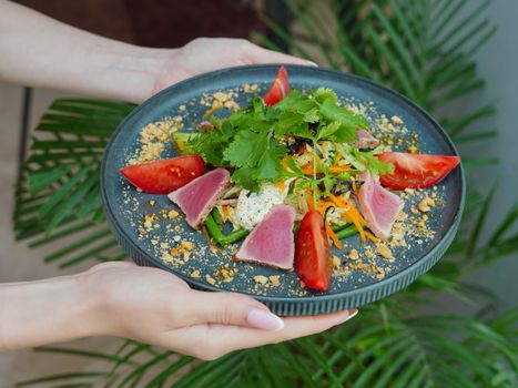 Delicious tuna salad with fresh vegetables and herbs served on a gray plate.