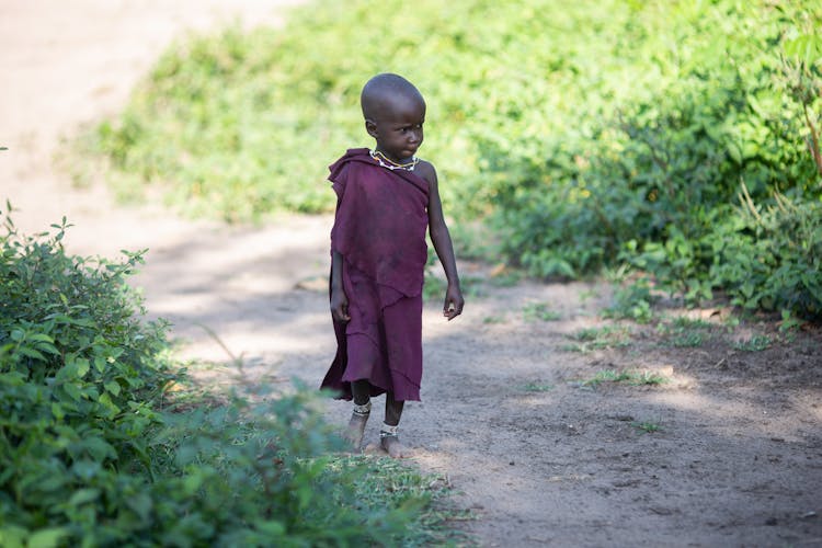 A Little Girl Walking Barefoot On A Dirt Road In The Countryside 