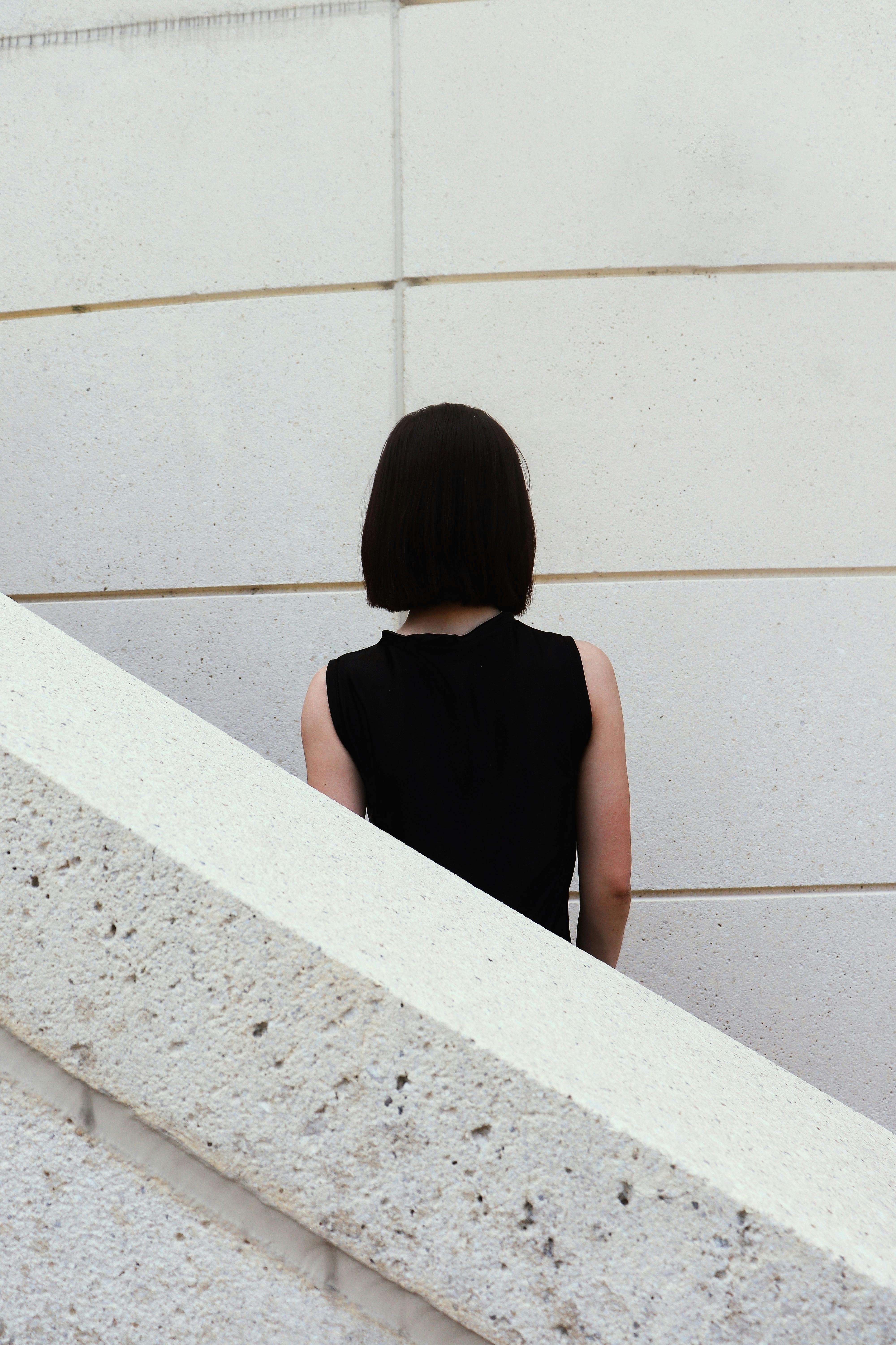 A woman stands with her back to a modern white wall in an urban setting.