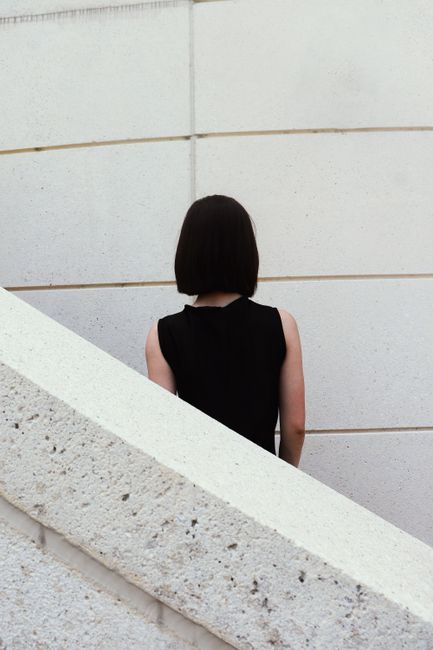 A woman stands with her back to a modern white wall in an urban setting.