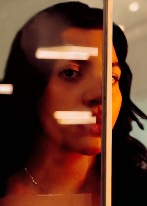 Free Artistic portrait of a woman partially obscured by reflections in glass creating a mysterious effect. Stock Photo