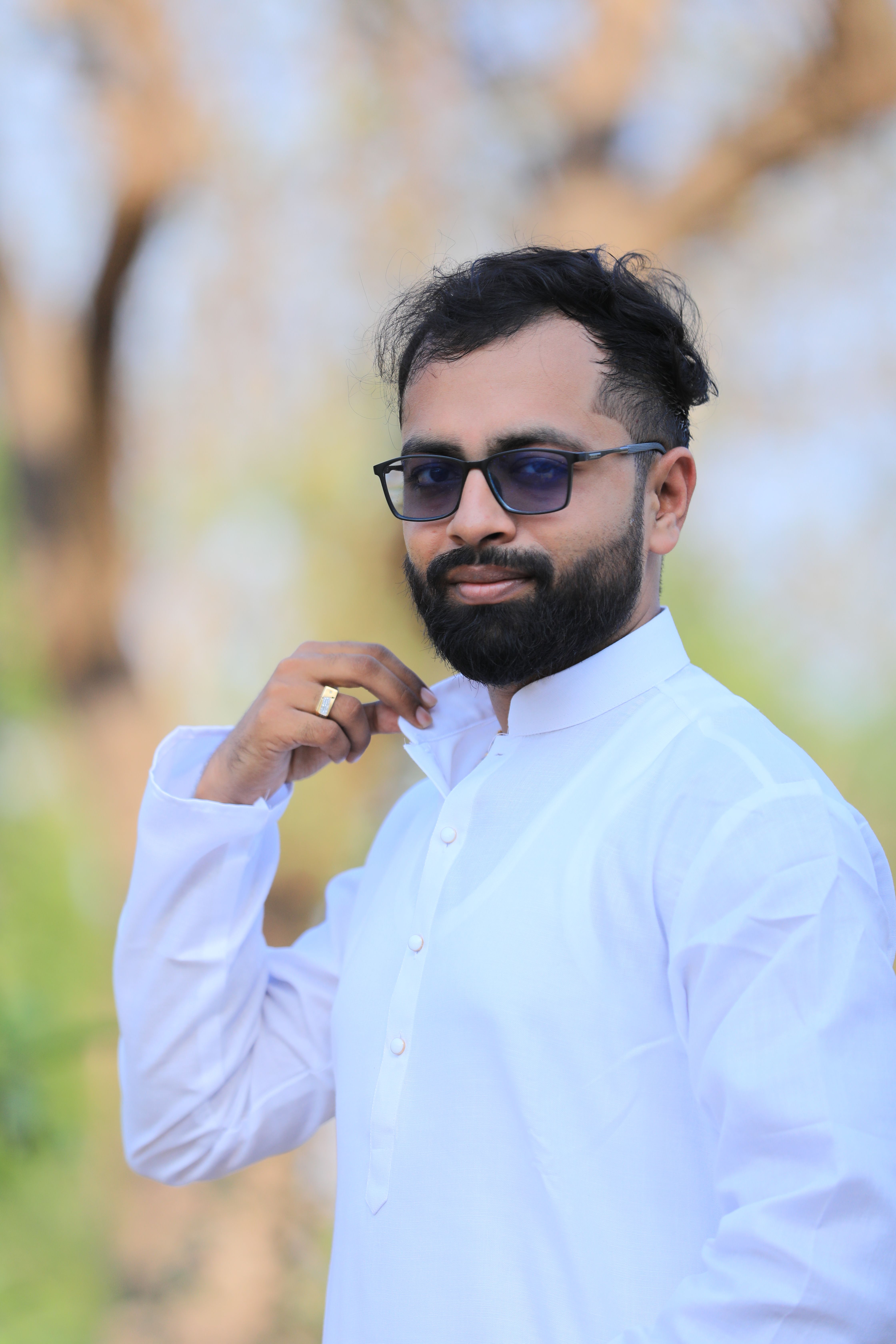 Portrait of a confident Indian man in a white kurta adjusting his collar outdoors.