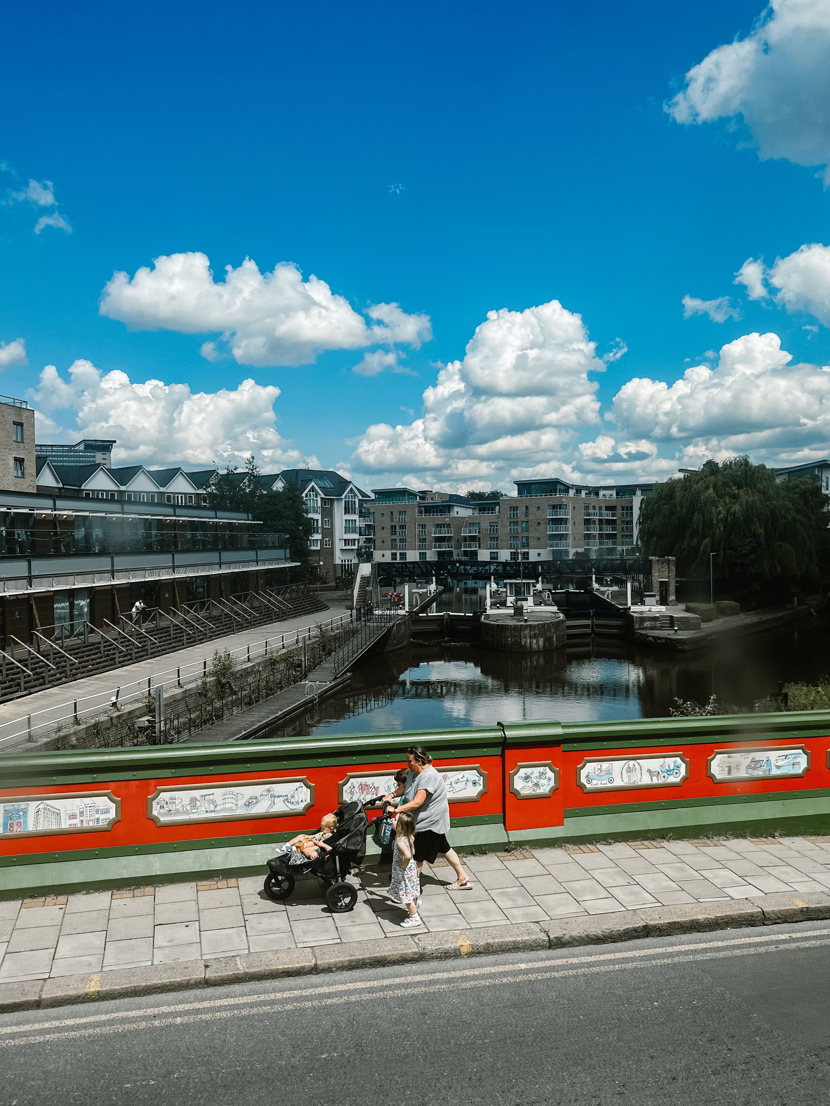 Family walking across a vibrant city bridge with scenic buildings and river in the background.