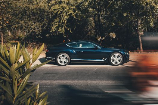 A sleek Bentley Continental GT parked on a shaded street in Chandigarh, India.