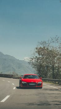 A sleek red Audi R8 speeds along a scenic mountain road in Shimla, India, showcasing luxury and performance.