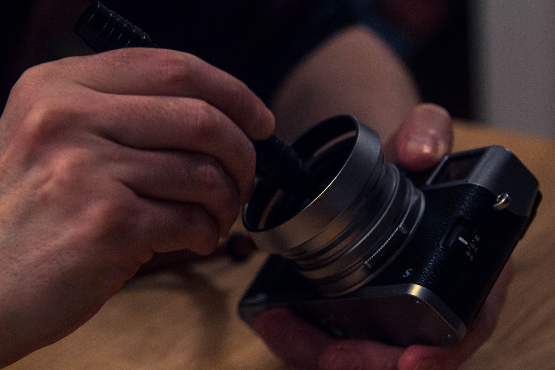 Close-up of hands cleaning camera lens with brush indoors, focusing on lens maintenance.