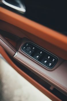 Close-up of a luxury car interior showing brown leather and control buttons on the door panel.