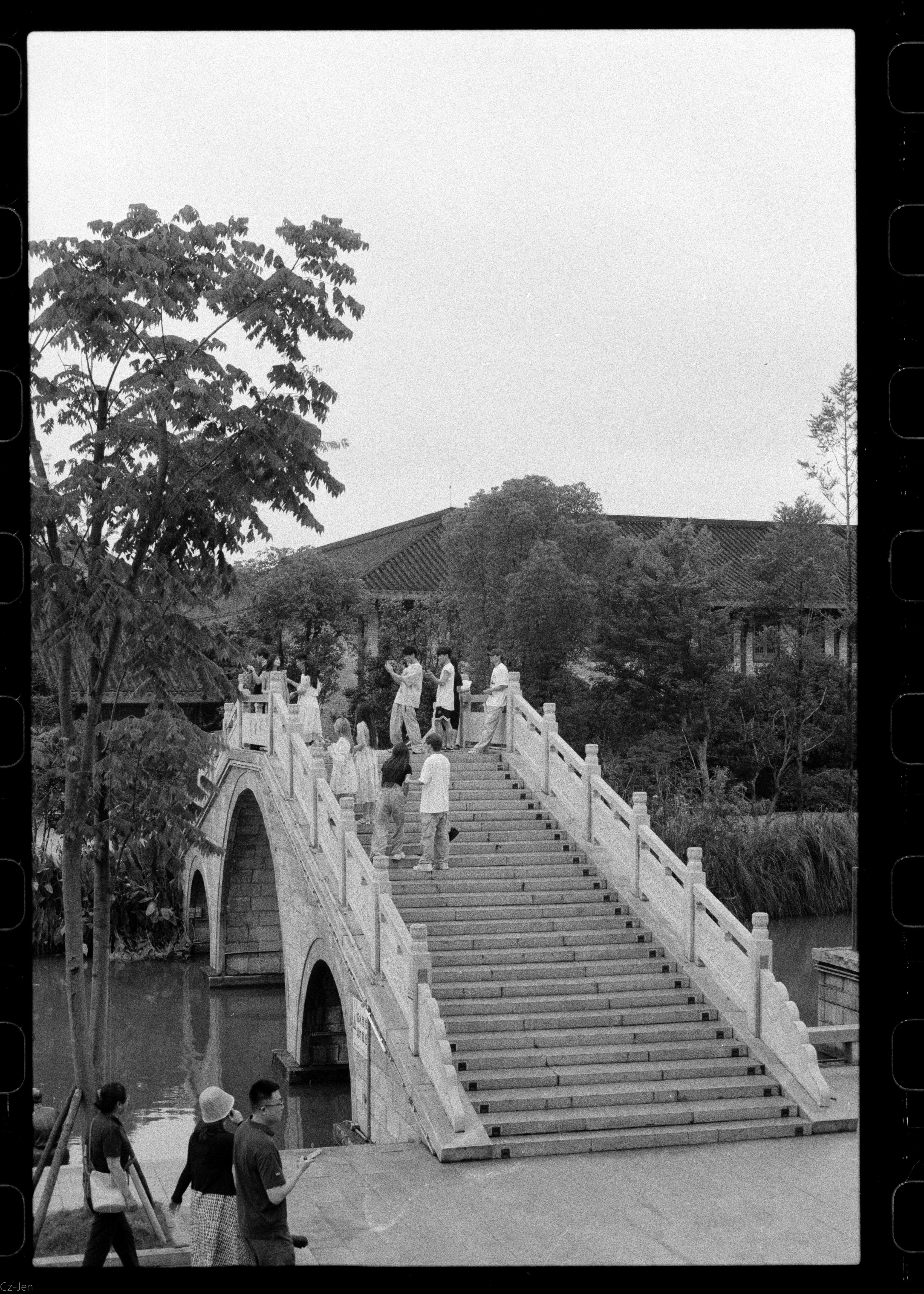 A classic stone footbridge with people crossing in a picturesque park setting.