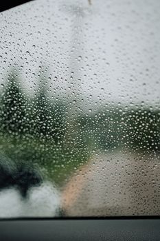 A close-up of raindrops on a window, blurring the outdoor scene for a moody atmosphere.