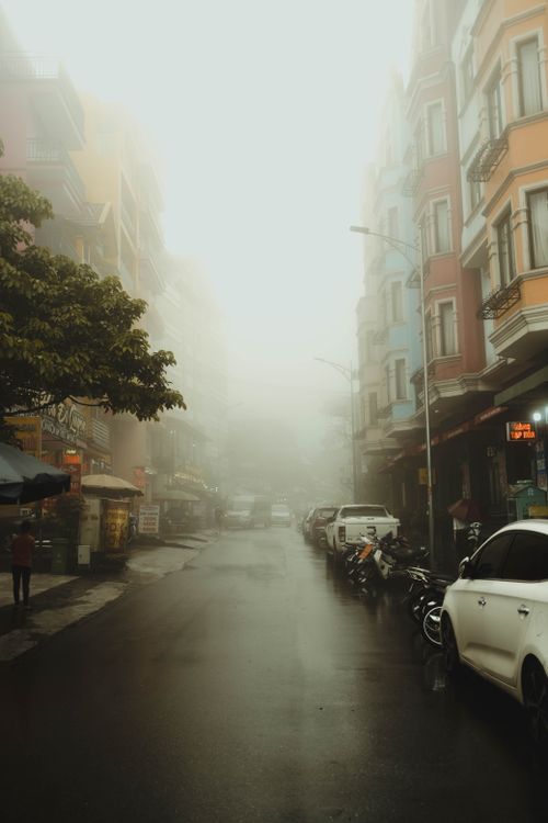 Free A foggy city street lined with colorful buildings and parked cars, creating a mysterious urban scene. Stock Photo