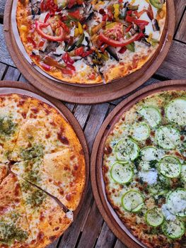 Three pizzas with diverse toppings served on wooden plates, showcasing food photography appeal.